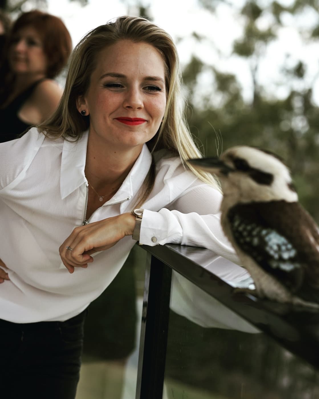 Denise leaning on a railing, smiling at a kookaburra perched beside her